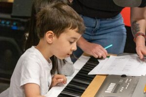 Backbeat Music Academy - boy writing songs at the piano while his teacher helps at backbeat music academy