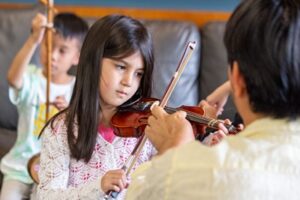 Backbeat Music Academy - girl playing the violin while her teacher assists at backbeat Music