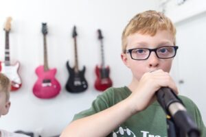 kid singing in front a wall of guitars at Backbeat Music Academy