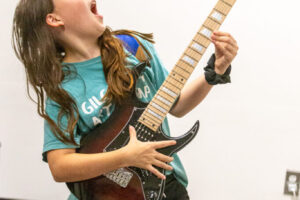 This is an image of a girl rock out out with a guitar and having a great time at a Backbeat Music Academy Summer Camp.