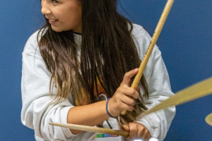 young girl plays a white drum kit in front of a blue wall